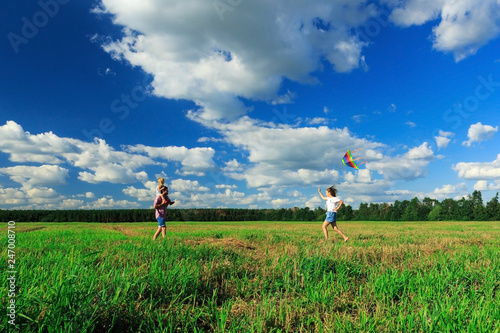Mother, father and daughter are flying a kite in the field.