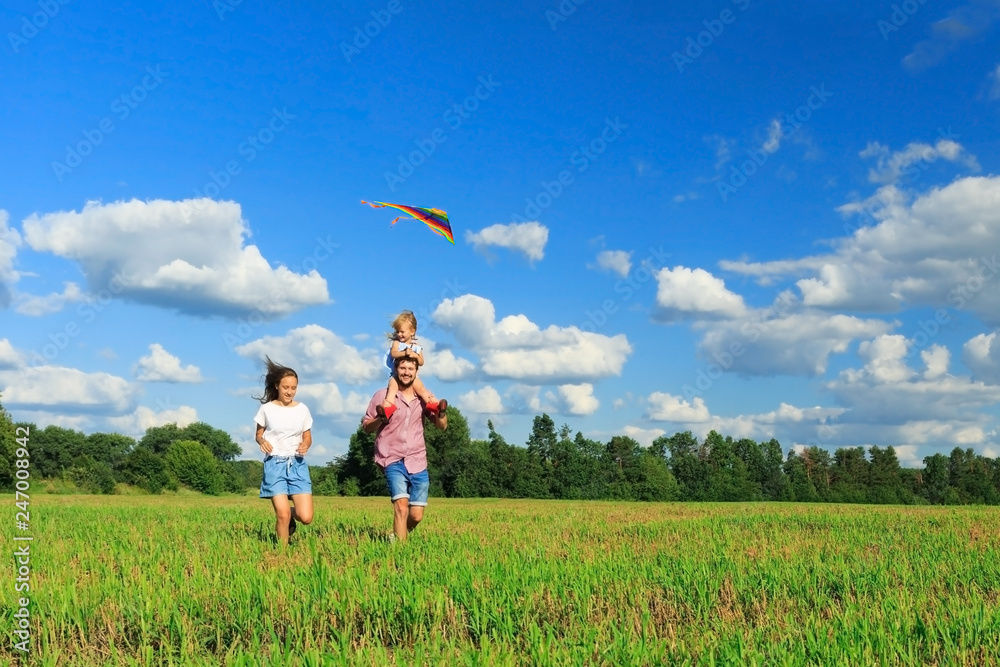Mother, father and daughter are flying a kite in the field. Front view, copy space. Mother, father and daughter are flying a kite in the field. Front view, copy space.
