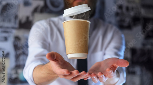 Levitating in the air paper cup with hot coffee. Barista, a bearded young man in a white shirt with a tie, creates miracles - advertises his drink, causing it to soar. Logoplacement concept