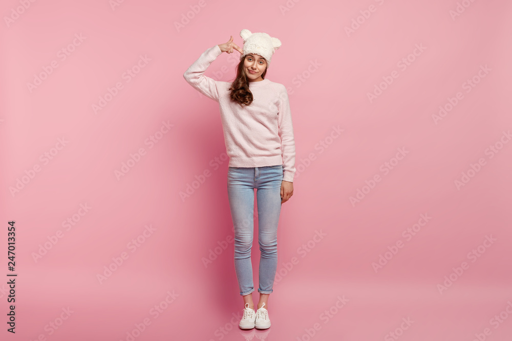 Slim beautiful woman imitates killing herself, keeps fingers on temples, wears casual outfit, feels fed up of boring life, stands indoor against pink background. Lady shoots in head. Suicide gesture Slim beautiful woman imitates killing herself, keeps fingers on temples, wears casual outfit, feels fed up of boring life, stands indoor against pink background. Lady shoots in head. Suicide gesture