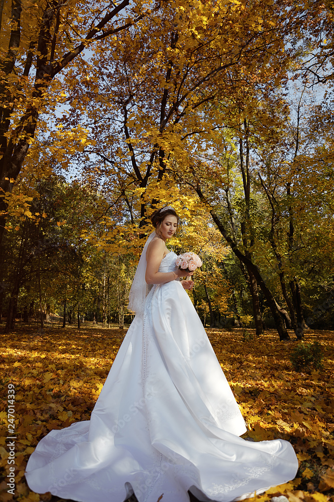 Beautiful bridesmaid dress with a long train. Autumn, fall of the leaves, a wedding dress developing in the wind.