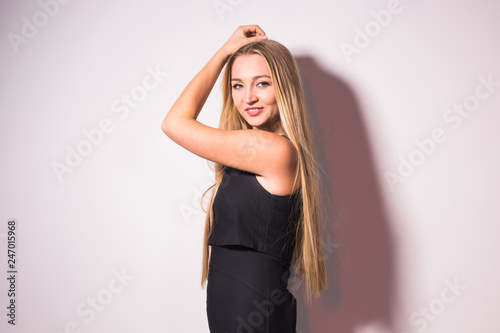 Fashion and model concept - Beautiful young sexy blond woman in a black dress posing against a white wall
