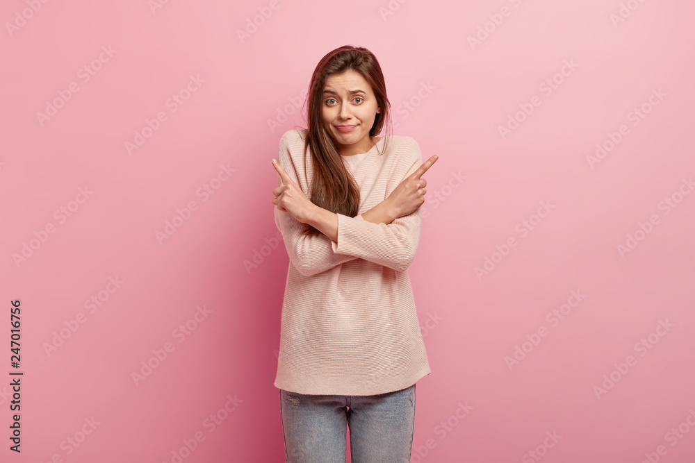 Photo of good looking woman with puzzled expression, crosses hands and points at different sides, has uncertain look wears casual jumper and jeans isolated over pink background. What to choose concept Photo of good looking woman with puzzled expression, crosses hands and points at different sides, has uncertain look wears casual jumper and jeans isolated over pink background. What to choose concept
