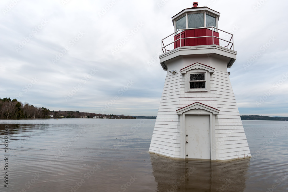 A lighthouse surrounded by water. Flood waters have risen part way up the door. Overcast sky.