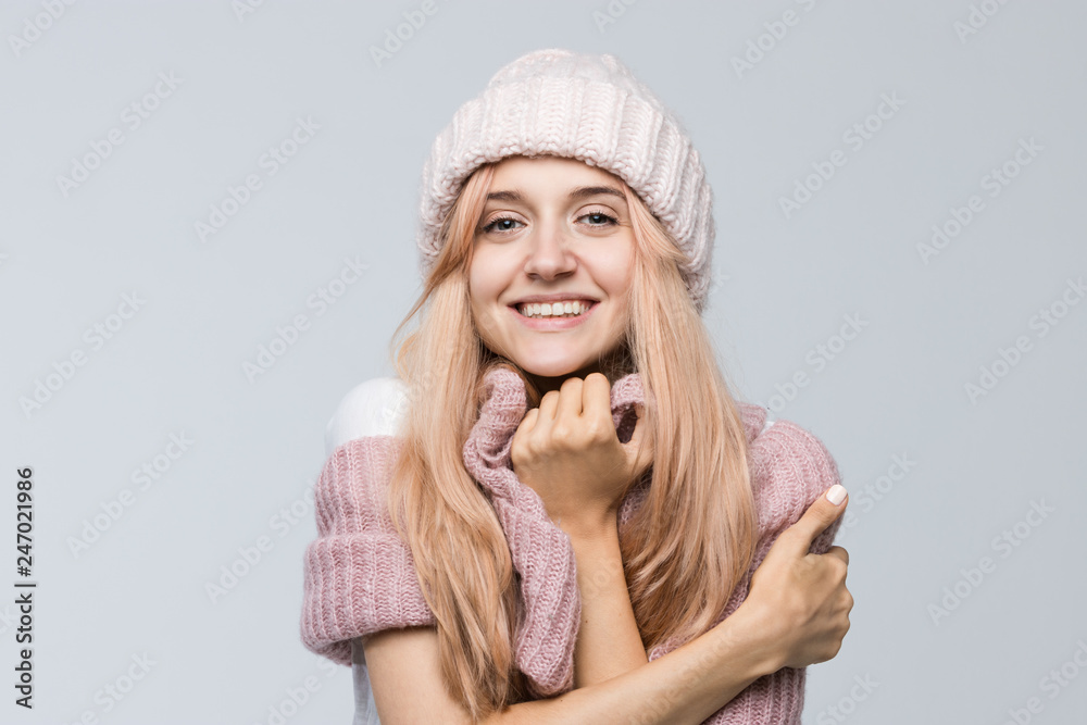 Studio portrait of attractive smiling female in pink sweater and white hat looking with satisfaction at camera, hugs herself/positive human facial expressions and emotions, perfect skin/people concept Studio portrait of attractive smiling female in pink sweater and white hat looking with satisfaction at camera, hugs herself/positive human facial expressions and emotions, perfect skin/people concept