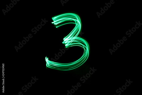 Long exposure, light painting photography.  Single number three in a vibrant neon green colour against a black background