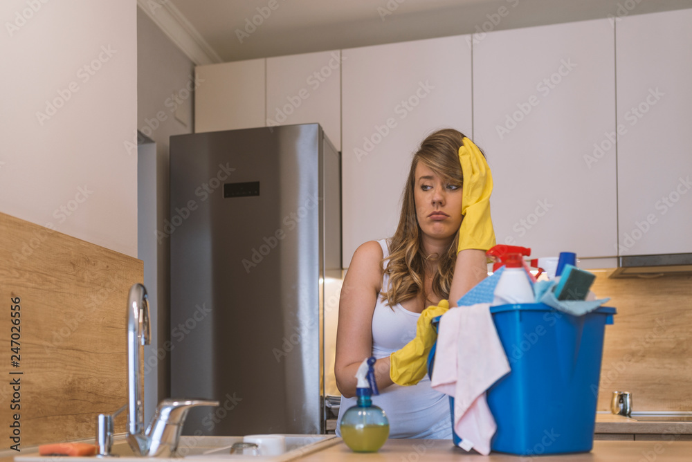 Φωτογραφία Frustrated woman with rubber gloves and apron holding basket with cleaning suppl