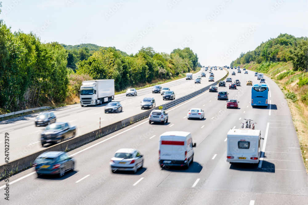 Heavy but fluid traffic on the eight-lane A10 highway in France in the direction of Bordeaux by a hot summer day with cars, vans, trailers, buses and semitrailer truck driving. - obrazy, fototapety, plakaty 