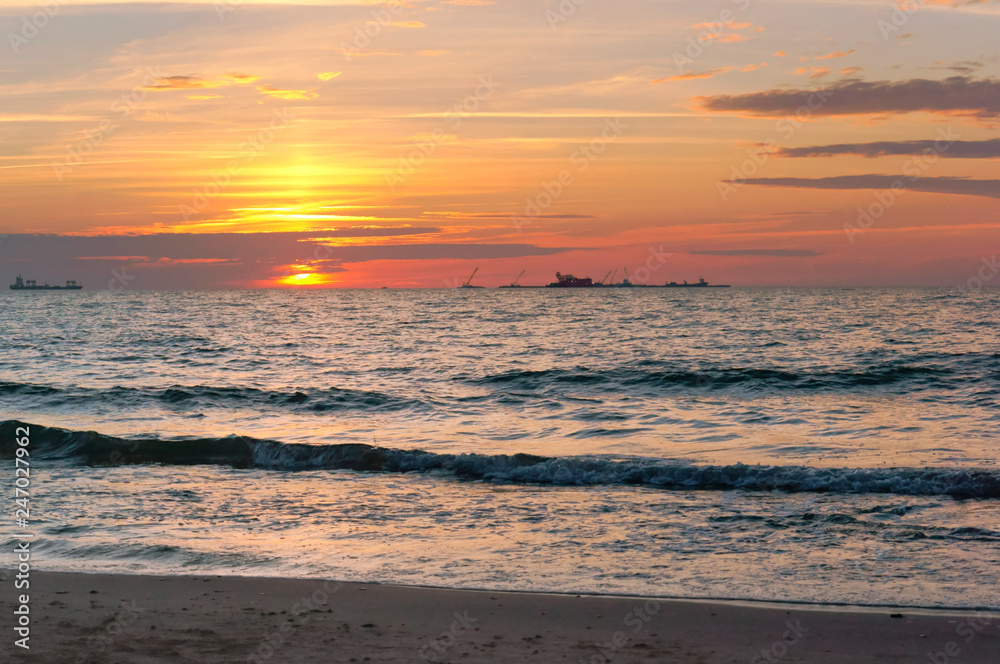 Sunset over the sea. Reflection of sunlight in the sea waves. Red and yellow sky in the rays of the sunset.