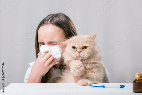 A girl holds a cat and blowing his nose in a paper handkerchief