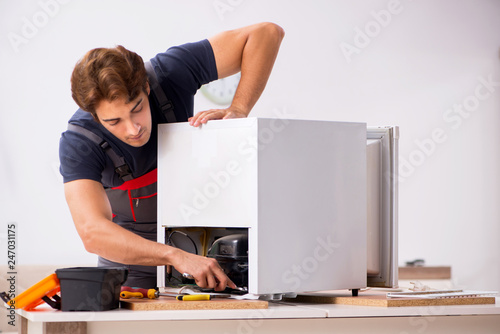 Young handsome contractor repairing fridge 