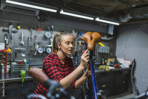 Technician woman fixing bicycle in repair shop. Young woman adjusting bike chain and repairing bicycle. Bike service