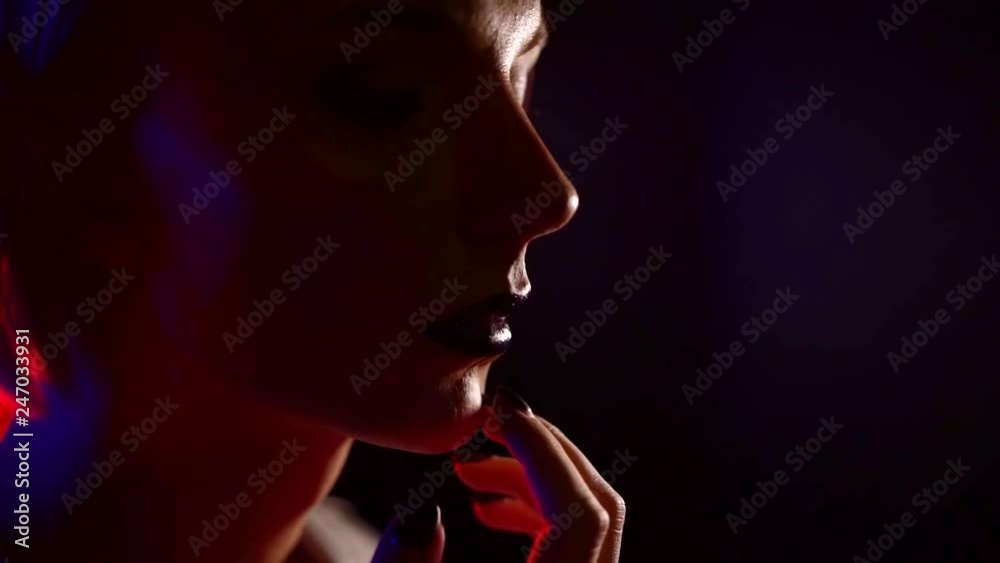 young woman is touching her face by fingers, close-up, she is standing alone in dark room young woman is touching her face by fingers, close-up, she is standing alone in dark room