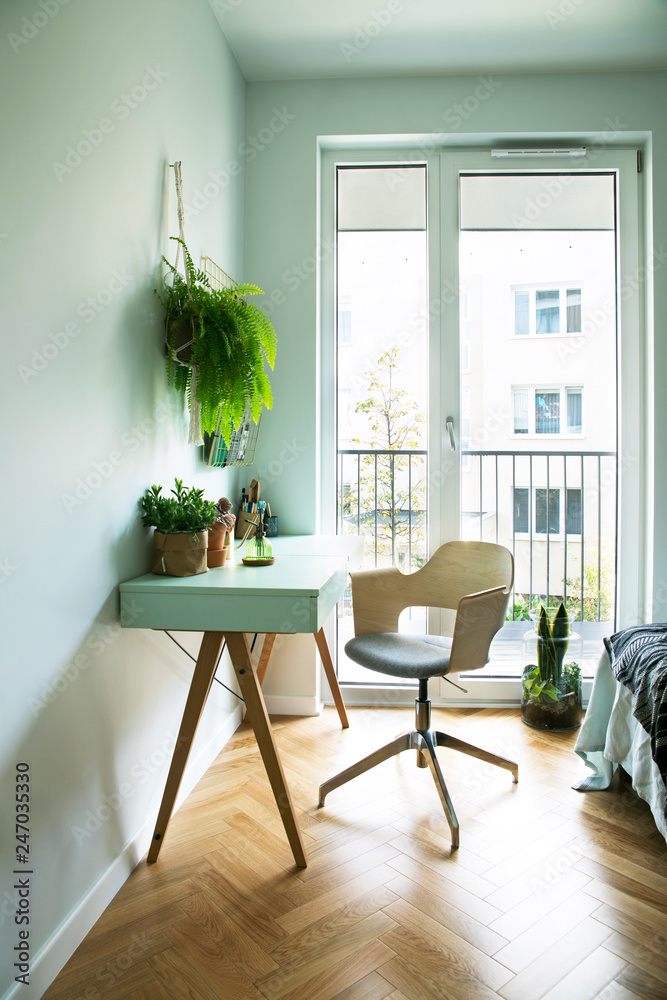 Modern scanidinavian interior of home office with design table, armchair, office accesories, big window and plants. Stylish and sunny space with wooden brown parquet. Modern scanidinavian interior of home office with design table, armchair, office accesories, big window and plants. Stylish and sunny space with wooden brown parquet.