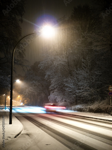 Car with motion blur driving on a snowy street with street lights at night