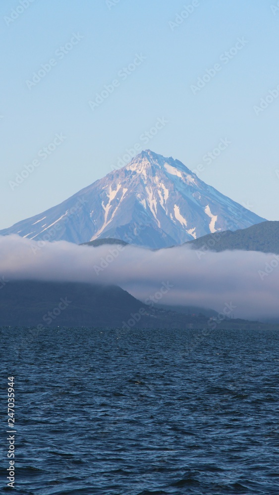 View of Vilyuchinsky volcano (also called Vilyuchik) from tourist boat. The cloud lies on the coastal cliffs. Vilyuchinsky is a stratovolcano in the southern part of Kamchatka Peninsula, Russia. View of Vilyuchinsky volcano (also called Vilyuchik) from tourist boat. The cloud lies on the coastal cliffs. Vilyuchinsky is a stratovolcano in the southern part of Kamchatka Peninsula, Russia.