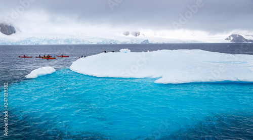 Huge iceberg with blue underwater part and small tourists kayaks with antarctic lagoon in the backgound, Peterman island, Antarctic peninsula photo