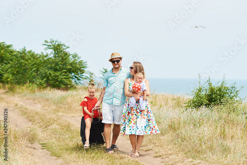Family, summer vacation, adoption and people concept - happy man, woman and daughters in sunglasses, with suitcases having fun over blue sky background 