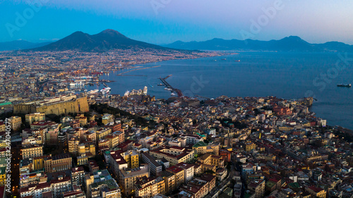 Aerial night view of Naples from the Vomero district. Castel Sant'elmo in the foreground while in the background the city's port, the Vesuvius and the Ovo castle. There are houses and buildings.
