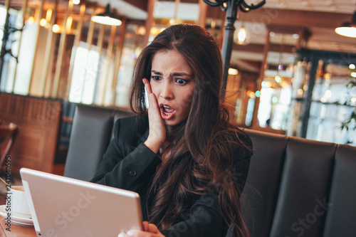 Beautiful charming brunette worried scared asian girl with tablet at table in cafe