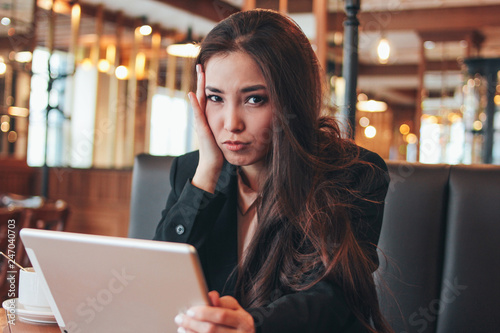 Beautiful charming brunette worried asian girl with tablet at table in cafe