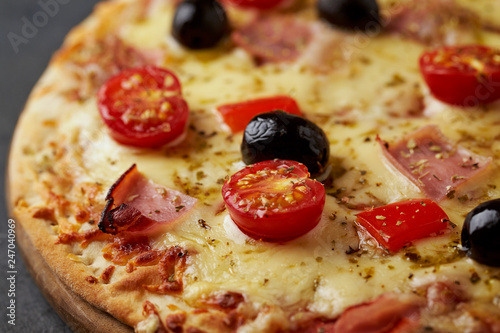 Pizza with ham, mozzarella cheese, cherry tomatoes, red pepper, black olives and oregano. Home made food. Concept for a tasty and hearty meal. Black stone background. Close up.