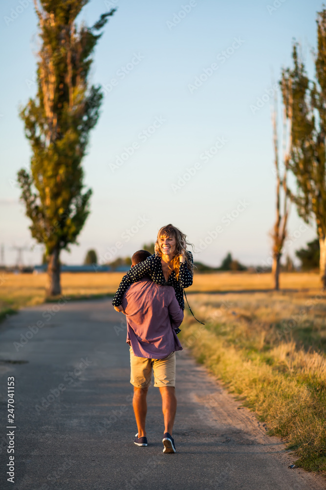 Enjoying beautiful day. Rear view of young cheerful man carrying his beautiful girlfriend on shoulder Enjoying beautiful day. Rear view of young cheerful man carrying his beautiful girlfriend on shoulder