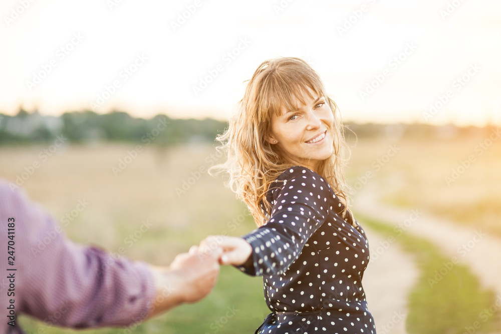Follow me. Young woman in straw hat holding boyfriend's hand walking in the field on sunset Follow me. Young woman in straw hat holding boyfriend's hand walking in the field on sunset