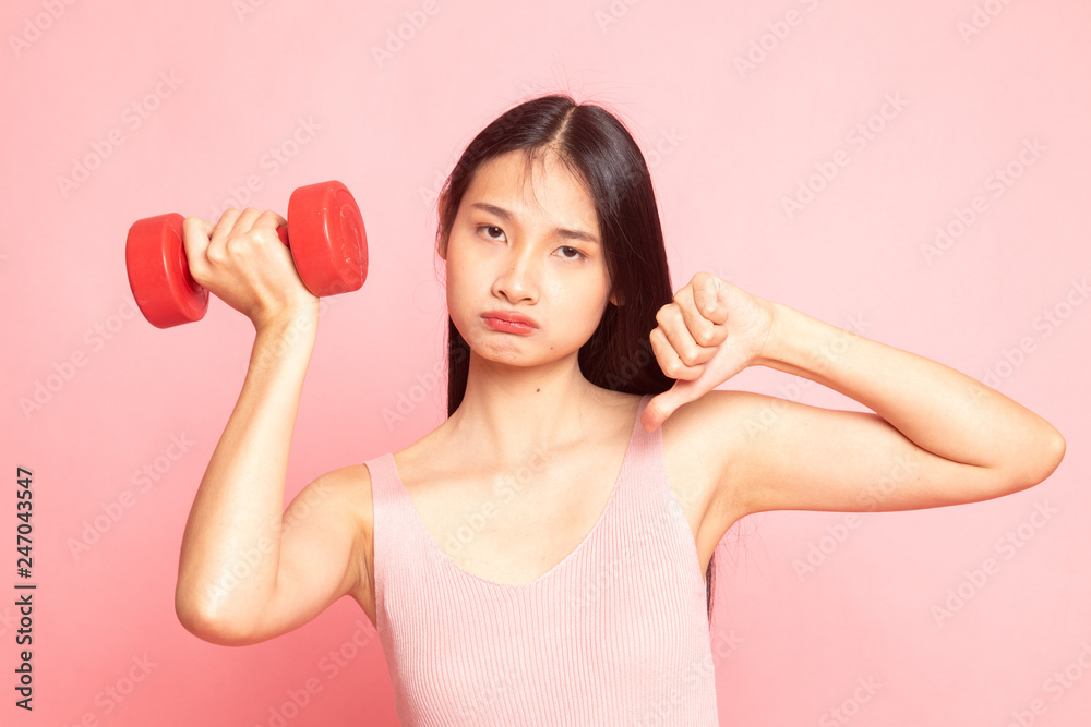 Unhappy Asian woman thumbs down with dumbbells. Unhappy Asian woman thumbs down with dumbbells.