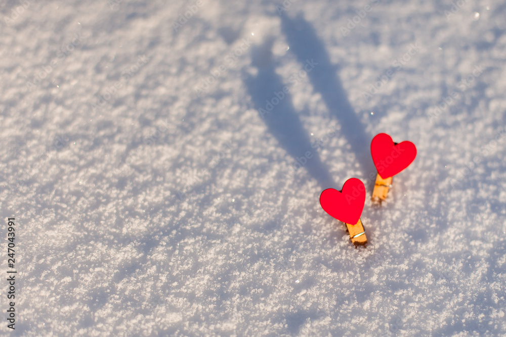 Two red decorative wooden hearts in white sparkling snow. Shadow. Sunny winter day. Located on the right.