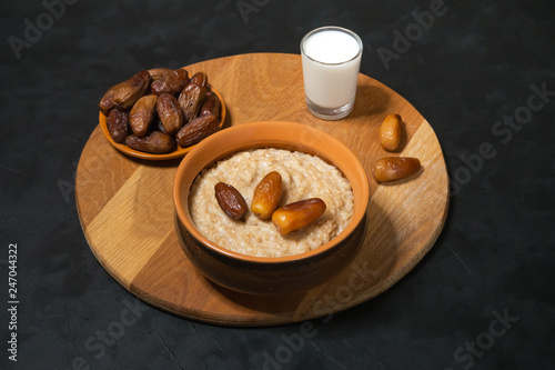 Healthy food. Oatmeal with dates with milk on the black table.