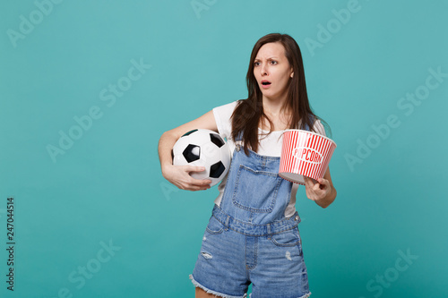 Puzzled young girl football fan watching match support favorite team with soccer ball, bucket of popcorn isolated on blue turquoise background. People emotions, sport family leisure lifestyle concept. photo