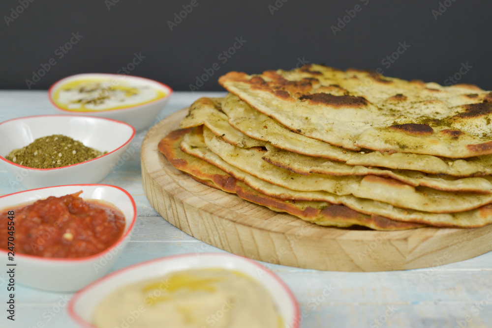 Traditional Indian Naan bread on wooden background with small plates of some salads : labneh , hummus and matbucha (Morrocan tomato salad) , flay lay top view with copy space Traditional Indian Naan bread on wooden background with small plates of some salads : labneh , hummus and matbucha (Morrocan tomato salad) , flay lay top view with copy space