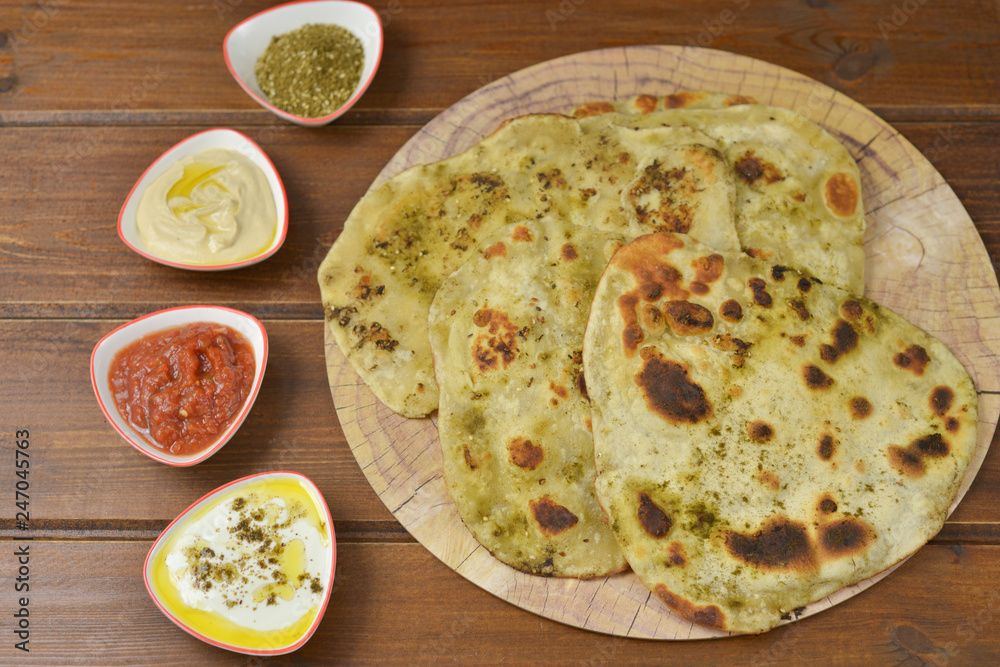 Traditional Indian Naan bread on  wooden background with small plates of some salads : labneh , hummus and matbucha (Morrocan tomato salad) , flay lay top view with copy space 