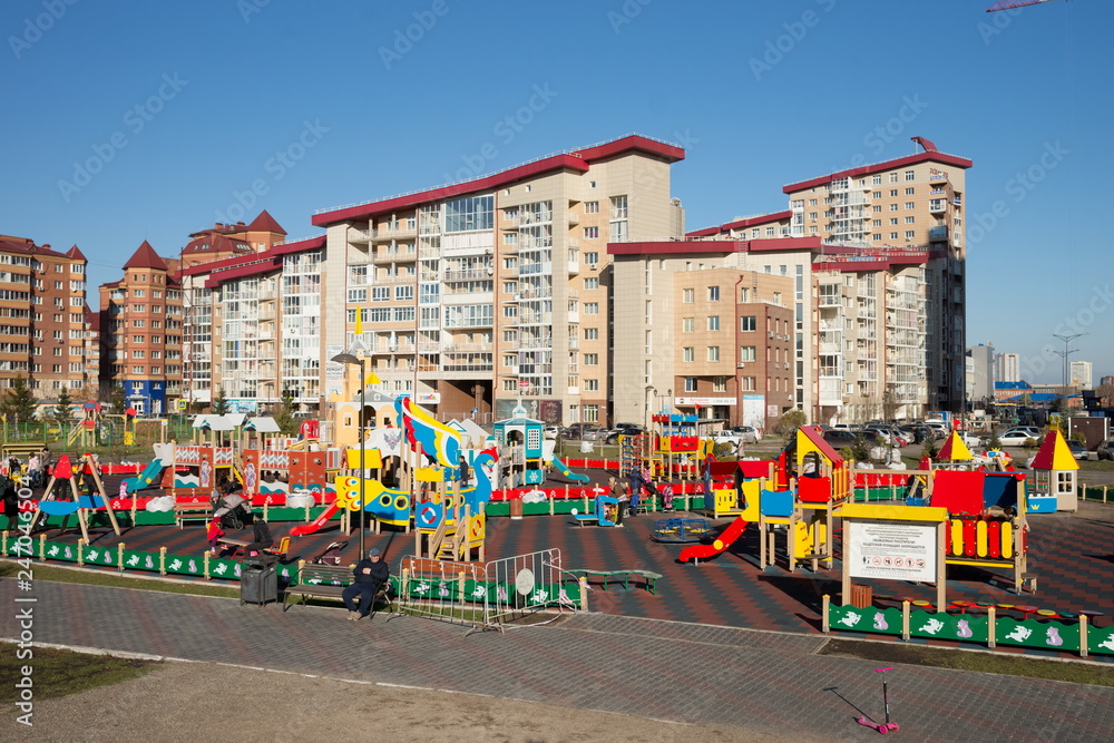 Kids with parents play on a public playground in a residential area of ​​Krasnoyarsk on a sunny autumn day.
