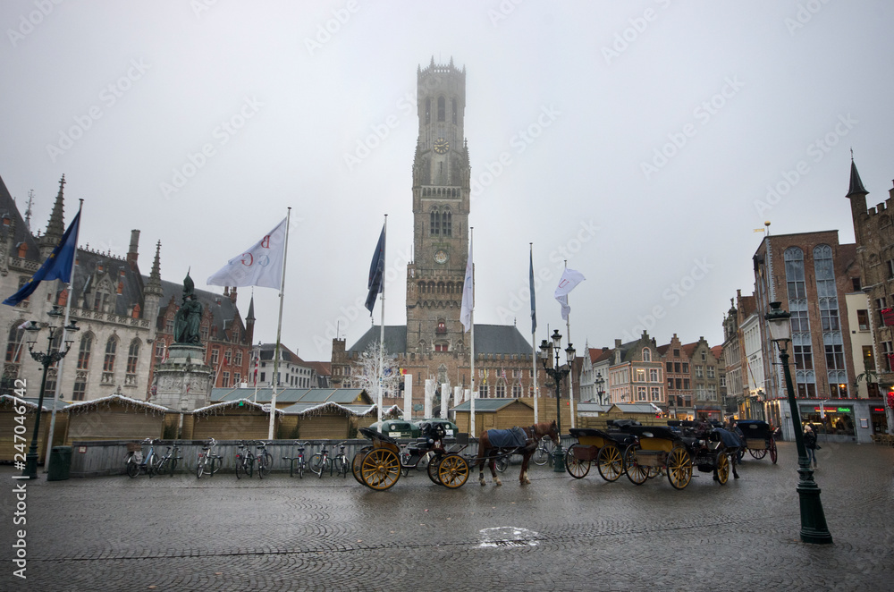 Fototapeta premium Bruges/Belgium - December 31 / 2016 : Horse carts are wating for the customers in front of Belfry of Bruges at Markt square
