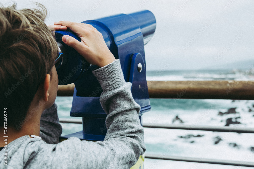 Close up view of a child looking horizon through blue telescope spyglass in front of ocean what we see far away watching the moon stars watch birds planes sky young boy looks through binoculars sea Close up view of a child looking horizon through blue telescope spyglass in front of ocean what we see far away watching the moon stars watch birds planes sky young boy looks through binoculars sea