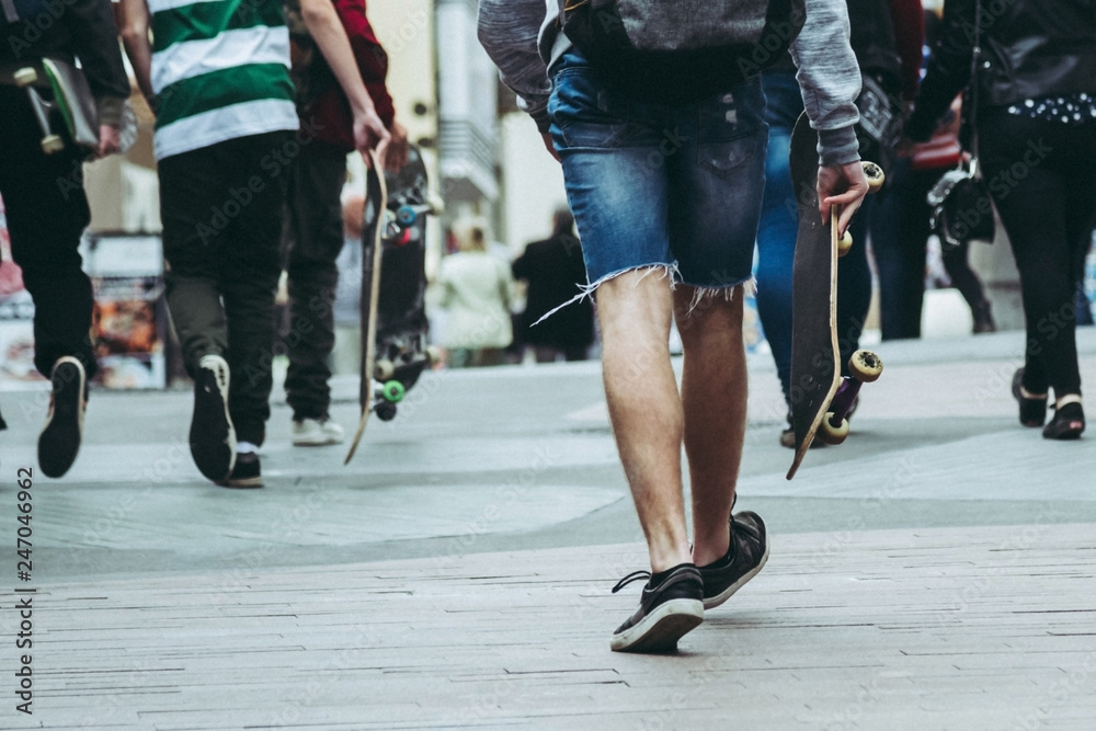 Teens walking and skateboarding through the streets of a urban city in a cloudy day enjoying the moment and having fun, a group of boys with skates visiting a modern town in the weekend. Trendy boy