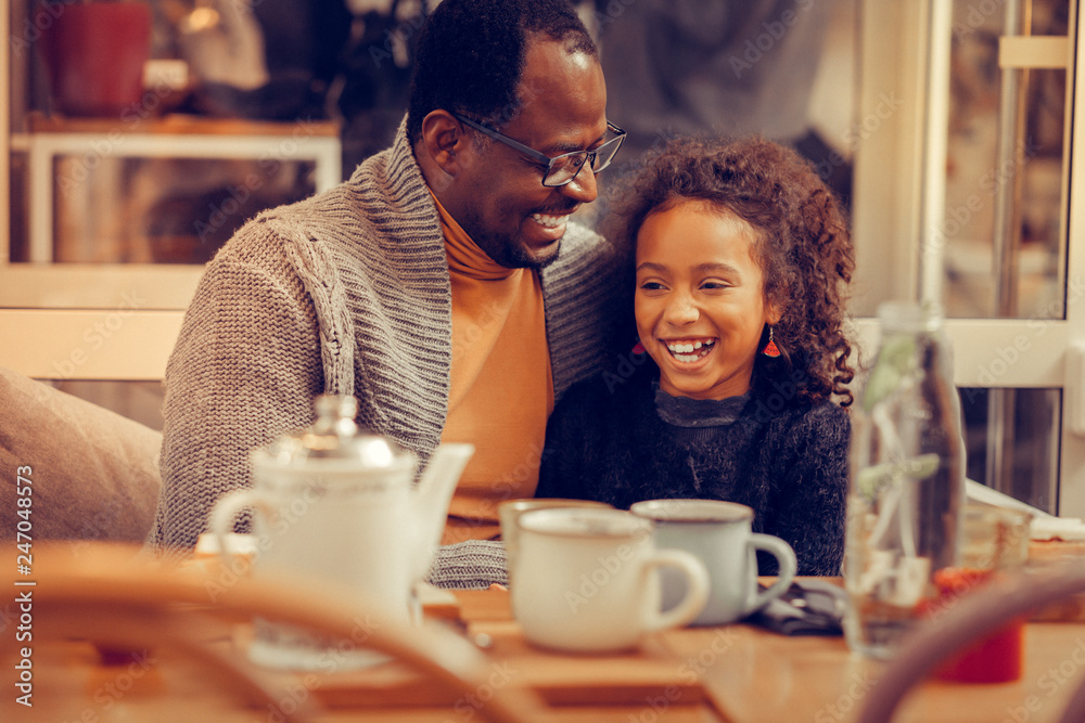 Cheerful cute curly daughter laughing while speaking with father Cheerful cute curly daughter laughing while speaking with father