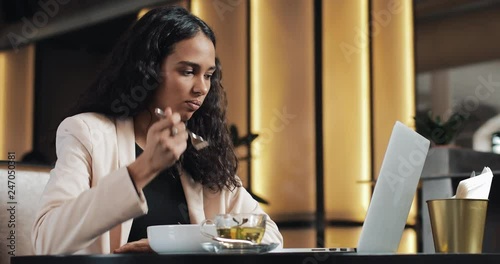 Business woman sitting with a laptop in the cafe and eating dinner with a cup of tea on the table. Eating lunch at work desk