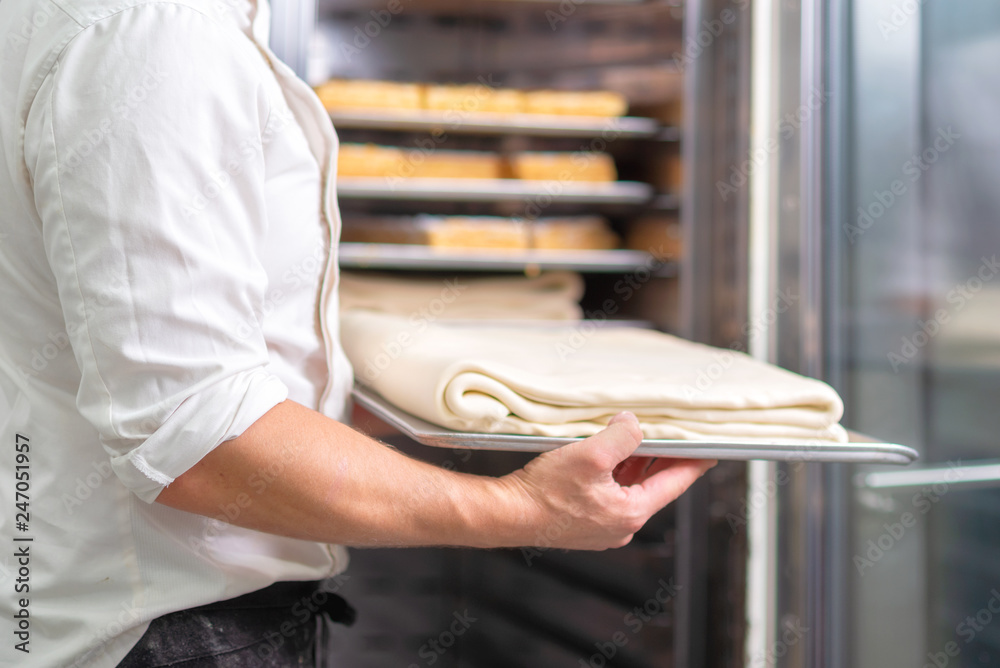 Pastry chef, putting the tray with dough into the fridge .