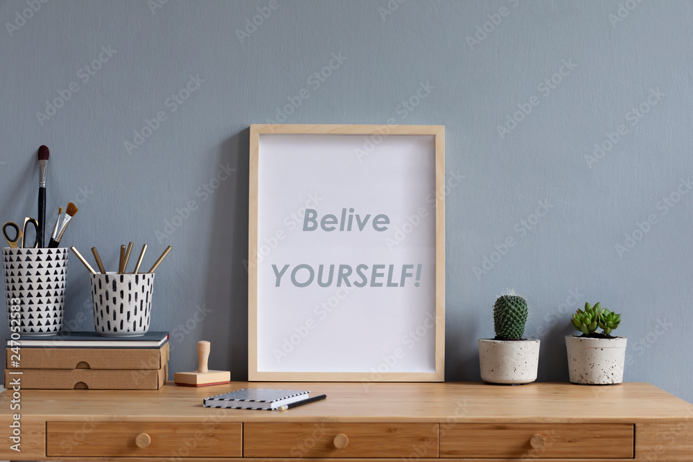 Obraz premium Scandinavian art interior with mock up photo frame on the brown wooden table with accessories, paper boxes,cacti in design pots, pencils brushes and pencils. Grey walls. Minimal concept of mockup.