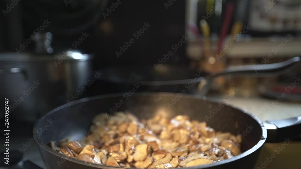 the hand of an old man salt the mushrooms that are fried in a skillet, close-up, staged warm light the hand of an old man salt the mushrooms that are fried in a skillet, close-up, staged warm light