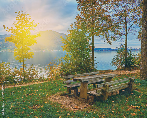 Beautiful scenic sunrise over calm and peaceful Austrian alps lake. Table and benches for tourists rest in the evening sunlight with clouds over alps mountains at the lake near Hallstatt Austria Alps © Vladimir V