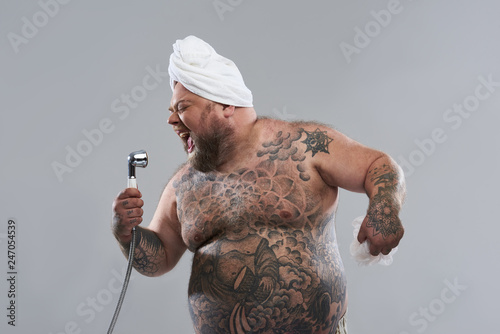 Enthusiastic tattooed man using shower head as his microphone