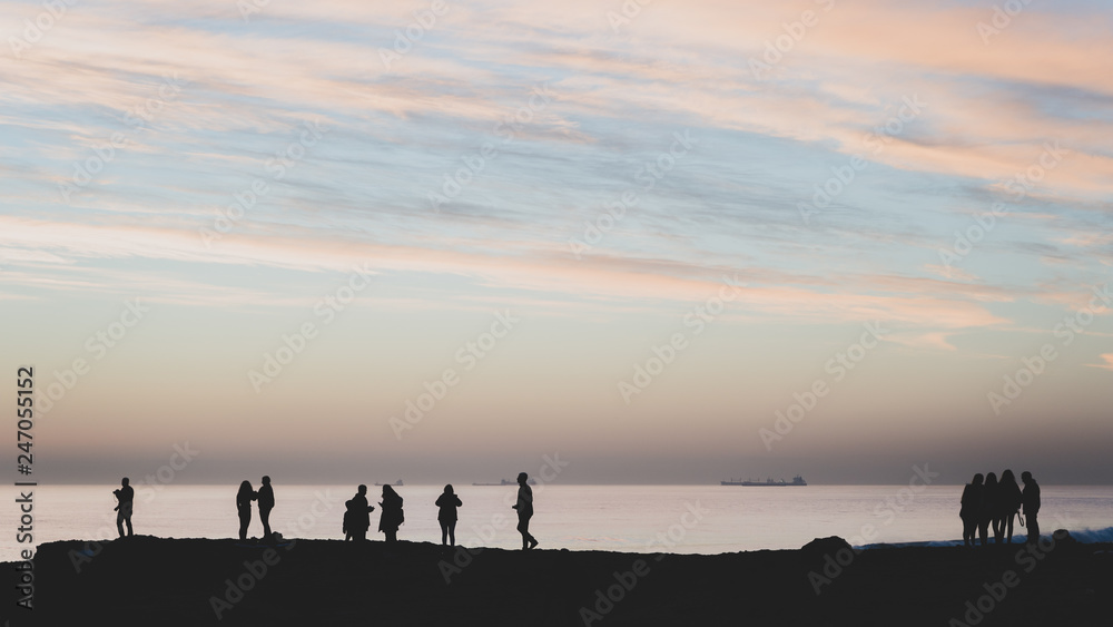 High contrast silhouettes of people at the beach facing the ocean on the horizon