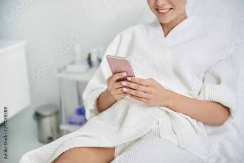 Joyful young lady using cellphone in spa salon