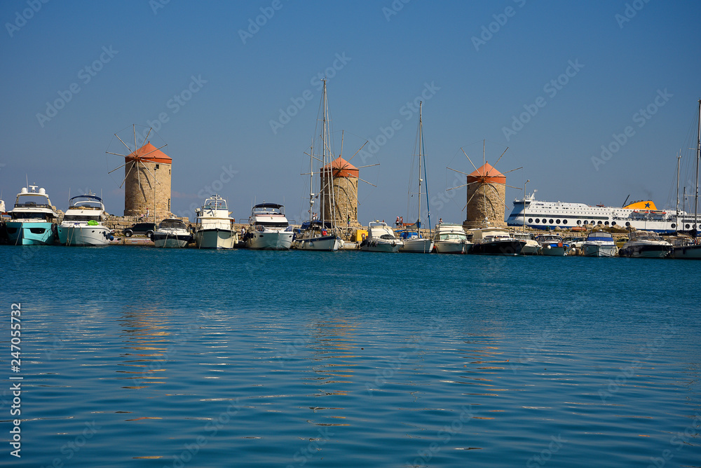 Fototapeta premium The windmills,fort of St Nikolas,Church of the Assumption and the Governors palace are on Rhodes Mandraki Harbour 
