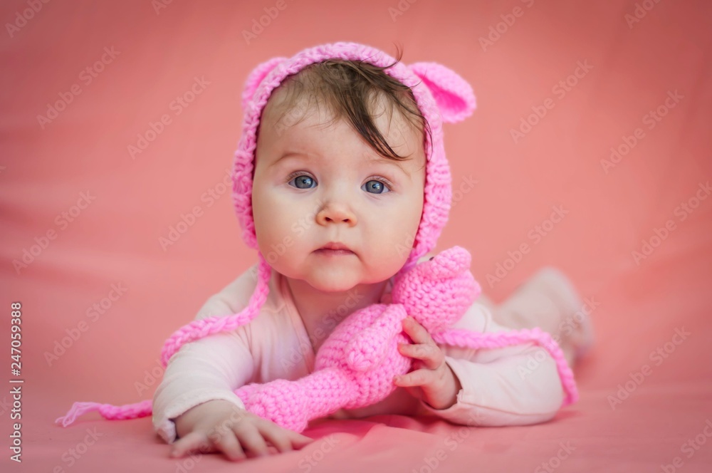 Cute and adorable six months old baby child lying on her belly and looking in the camera with a pink teddy bear and pink background. Cute and adorable six months old baby child lying on her belly and looking in the camera with a pink teddy bear and pink background.