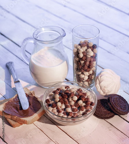 Chocolate cereal balls , jug of milk, biscuits and marshmallows on the wooden table photo